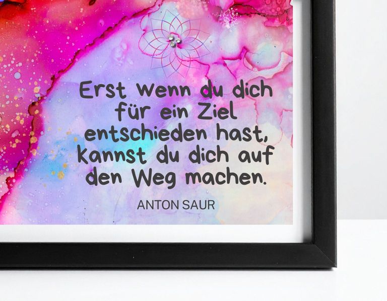 Ein dekorativer Kunstdruck mit einem abstrakten, farbenfrohen Hintergrund in Pink-, Rot- und Lila-Tönen und einem inspirierenden deutschen Zitat von Anton Saur über Zielsetzung, gerahmt in einem schwarzen Rahmen.